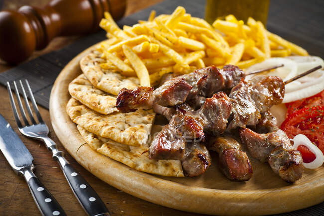 Греческая свинина сувлаки с жареным картофелем и хлебом на гриле — стоковое фото