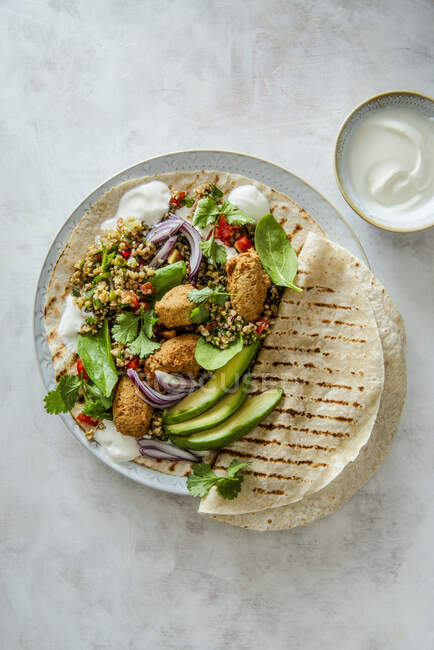 Envoltura con tabbouleh y falafels, yogur griego, aguacate, espinacas y cilantro - foto de stock