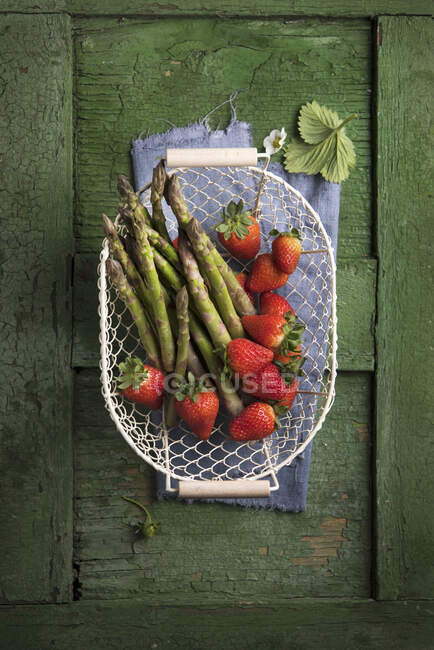 Espargos e morangos em uma cesta de arame em uma superfície de madeira verde — Fotografia de Stock