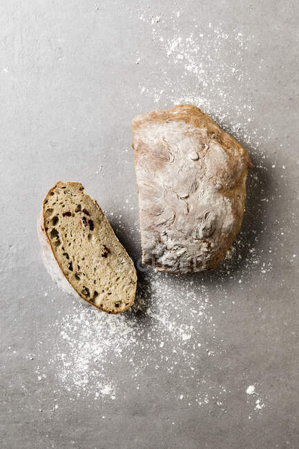 Bread with cranberries and pumpkin seeds, cut on stone surface with flour — Stock Photo
