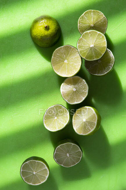 Primer plano de deliciosas mitades de lima en una superficie verde - foto de stock