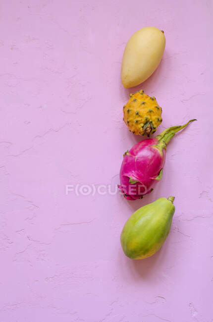 Verschiedene exotische Früchte in Reihe auf rosa Oberfläche — Stockfoto