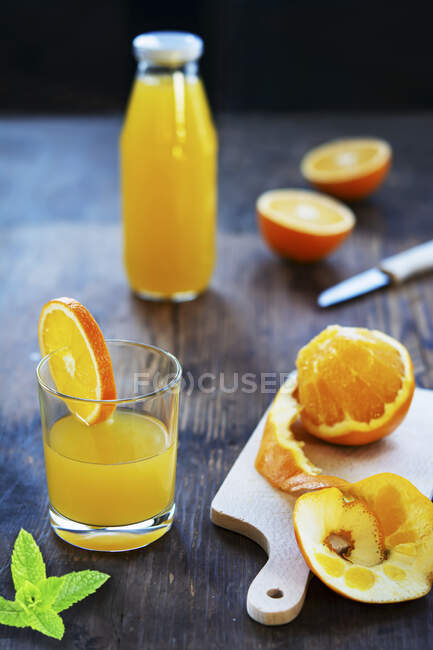 Jugo de naranja en un vaso y botella con naranjas frescas y hojas de menta - foto de stock