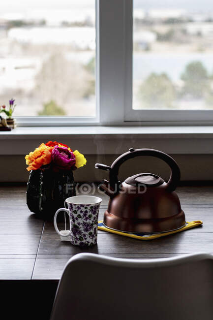 Xícara de chá, chaleira de chá e um vaso de flores em uma mesa na frente de uma janela — Fotografia de Stock