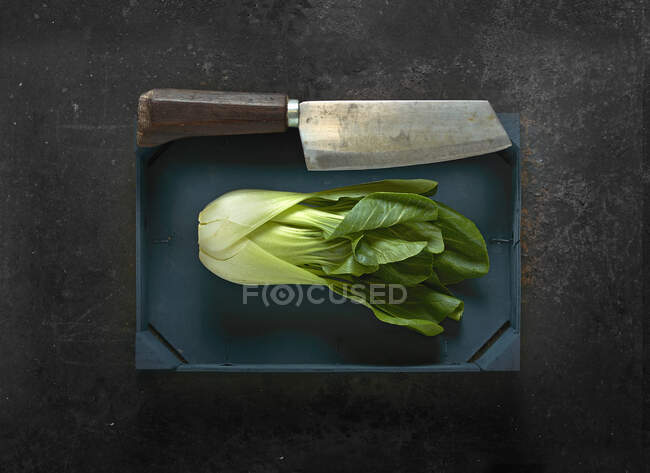 Bok choy in a wooden crate with a meat cleaver — Stock Photo