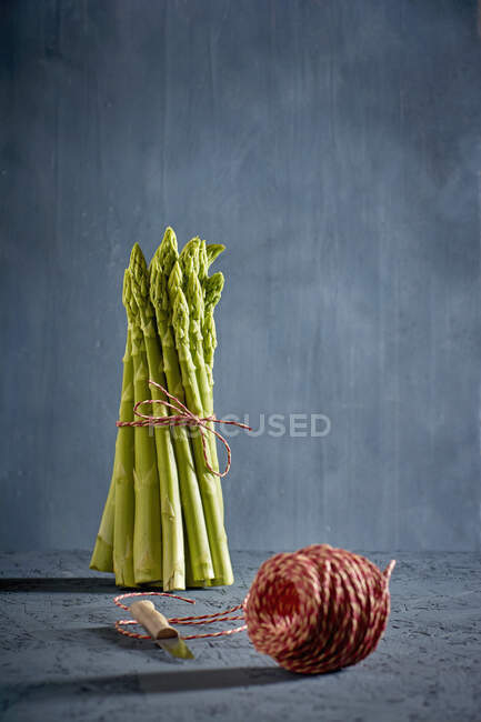 A bundle of green asparagus with a ball of kitchen twine in the foreground — Stock Photo