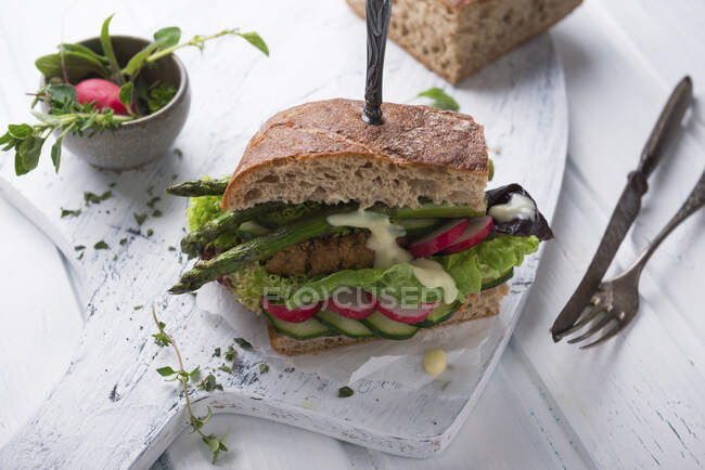 A sandwich with a bean patty, vegetables, lettuce, grilled asparagus and vegan Hollandaise — Stock Photo