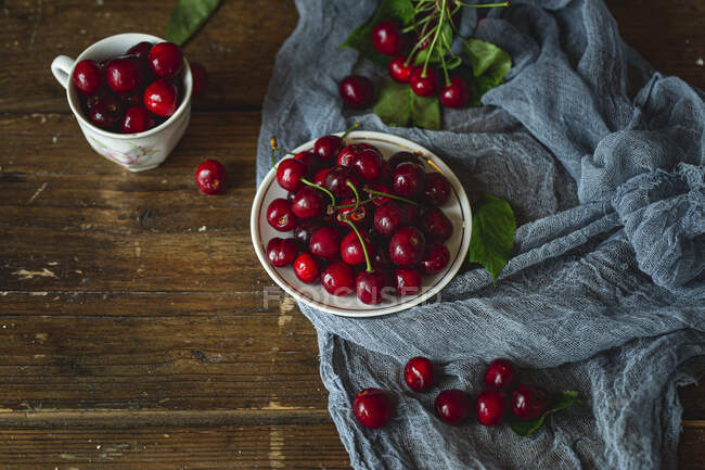 Fresh cherries with green leaves on cloth and on wooden table — Stock Photo