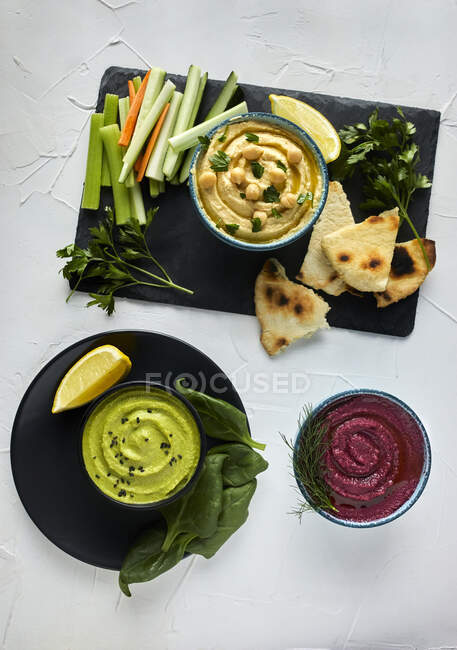 Various types of hummus served with fresh vegetables and pita bread — Stock Photo