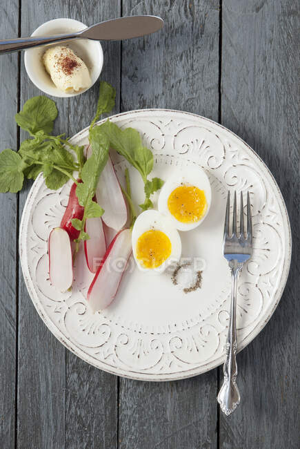 Soft boiled egg halves with radish, salt and pepper, herbs and butter in mini bowl — Stock Photo
