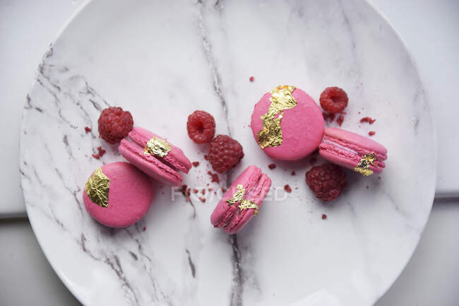 Pink macarons with raspberries and gold leaves — Stock Photo
