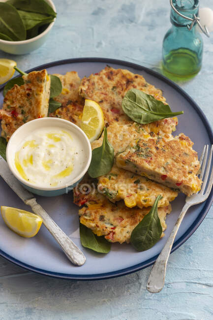Chicken, red pepper and corn fritters, yogurt with olive oil and pepper, lemons, spinach leaves — Stock Photo