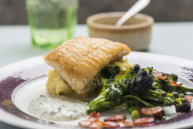 Fried fish on bed of mashed potatoes with broccolini and herb sauce — Stock Photo