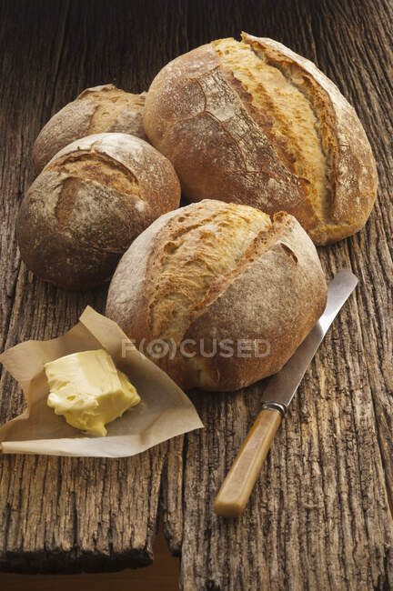 Panes de pan con mantequilla en papel y cuchillo en superficie de madera - foto de stock