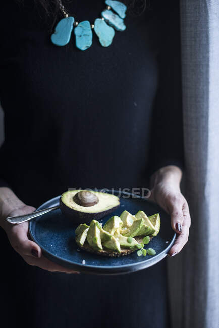 Una donna con in mano un piatto di pane all'avocado — Foto stock