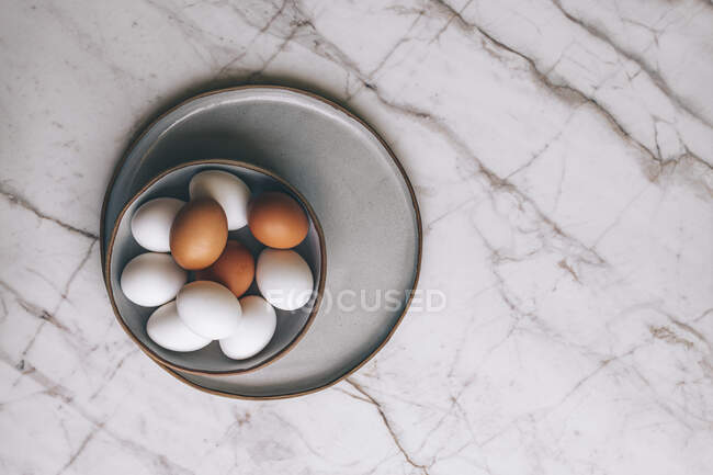 Mixed colour eggs in bowl on marble surface — Stock Photo