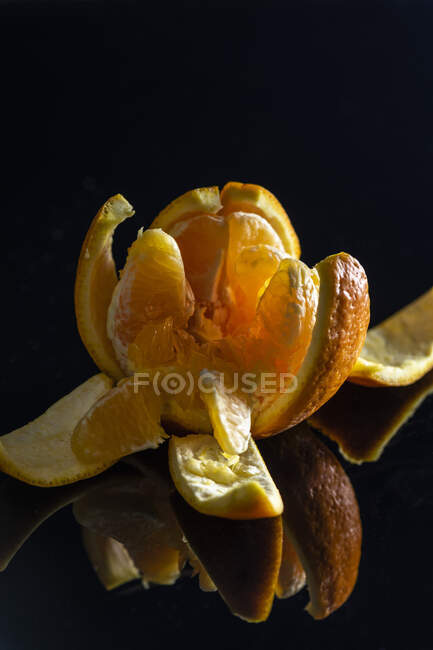A peeled orange broken into segments against a black background — Stock Photo