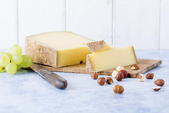 Hard cheese, hazelnuts and grapes on wooden board — Stock Photo