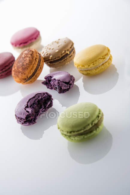 Ganze und rissige bunte Macarons mit Reflexionen auf weißem Hintergrund — Stockfoto