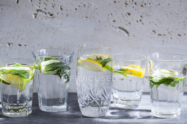 Vários copos de água cheios de limões, limas, hortelã e gengibre — Fotografia de Stock