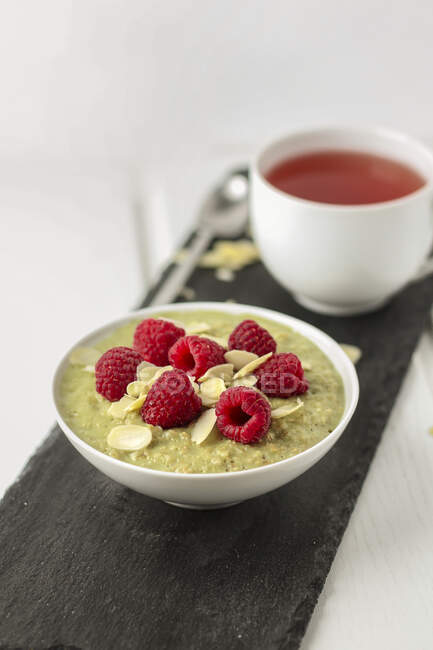 Matcha porridge with raspberries and almonds flakes and tea cup — Stock Photo