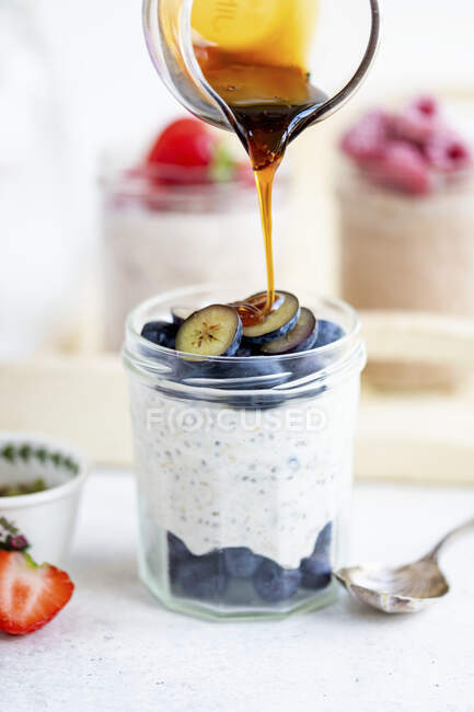 Overnight oats with blueberries and dripping syrup from glass jug — Stock Photo