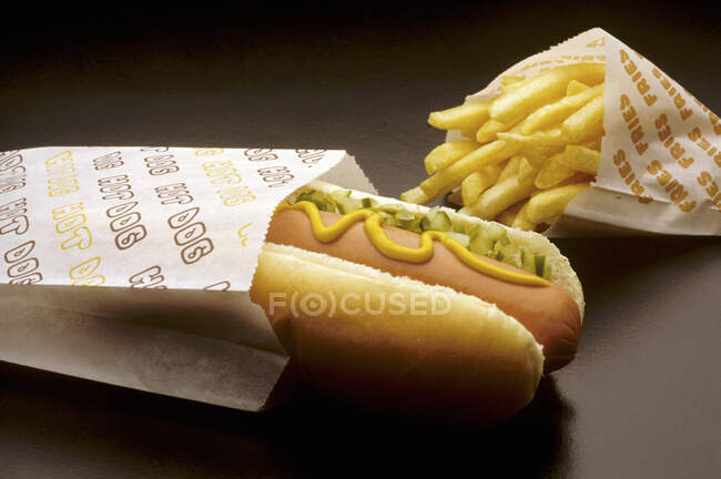 Hot dog vendeur de rue avec moutarde, cornichons et un sac de frites — Photo de stock