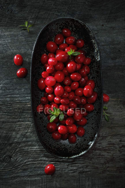 Fresh cranberries with green leaves in bowl and on wooden table — Stock Photo