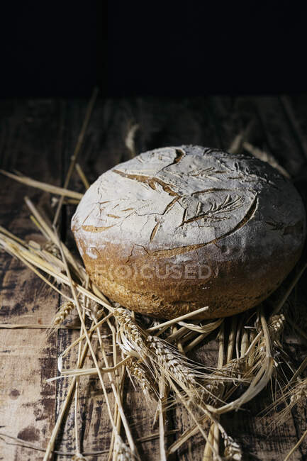 Homemade bread loaf on wheats at wooden surface — Stock Photo