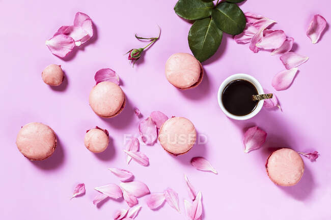 Рожеві макаруни з пелюстками троянд та чашкою кави — стокове фото