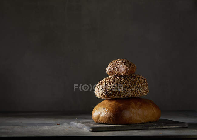Deux pains et un rouleau de pain, empilés sur fond sombre — Photo de stock