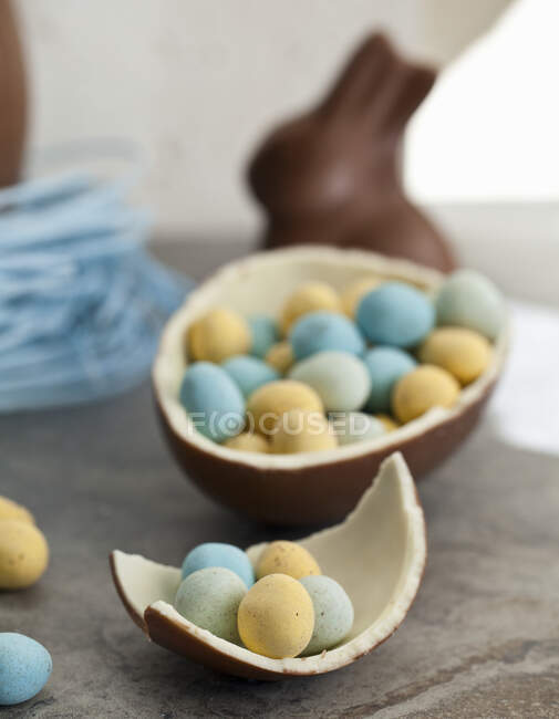 Osterschokoladenei in einem Nest mit Blaubeeren und einem Schokoladenhasen und einem halbierten Schokoladenei, das mit Mini-Schokoladeneiern gefüllt ist — Stockfoto
