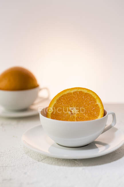 Metades de laranja em copos brancos — Fotografia de Stock