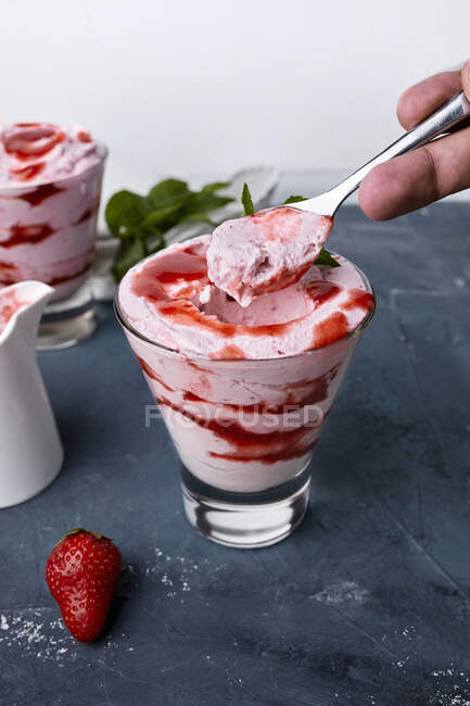 Hand holding spoonful of Strawberry mousse, dessert in glasses with fresh strawberry on table — Stock Photo