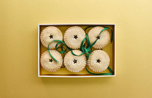 Petites tartes hachées en boîte sur fond jaune — Photo de stock