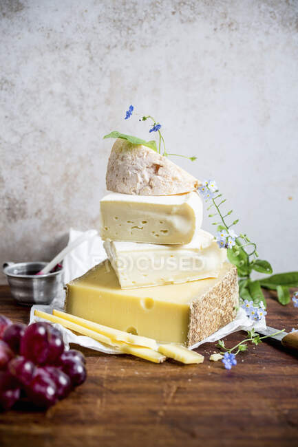 Различные сорта сыра, укладываемые цветами и виноградом на деревянной поверхности — стоковое фото