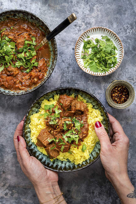 Main tenant assiette de curry de boeuf avec du riz safran à côté des bols — Photo de stock