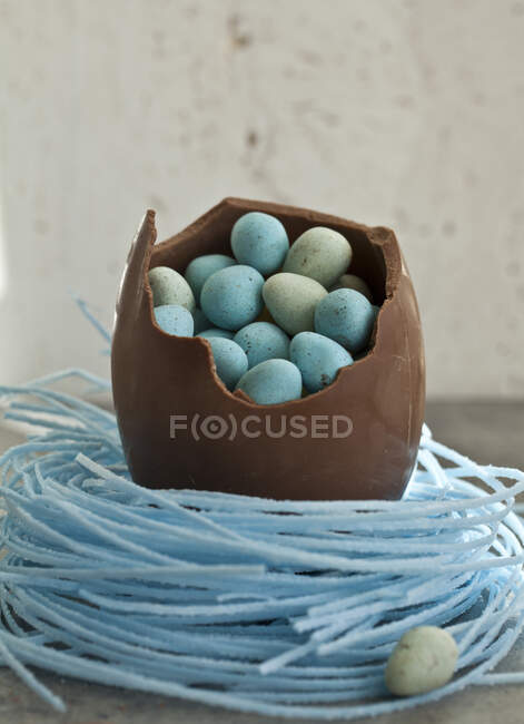 Велике шоколадне яйце Пасхи, яке лежить у чорнильниковому гнізді, наповнене крихітними шоколадними яйцями. — стокове фото
