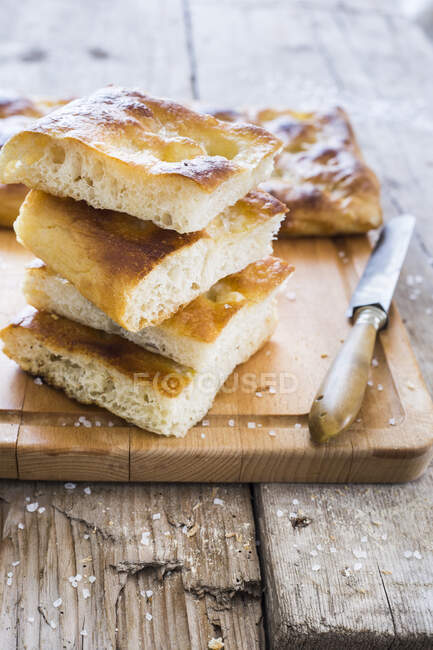 Focaccia genovese sliced and stacked on wooden board with knife — Stock Photo