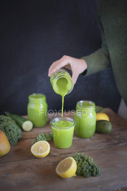 A woman pours green smoothies into glasses — Stock Photo