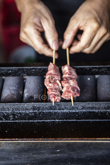 Hände halten Spieße auf japanischem Grill — Stockfoto