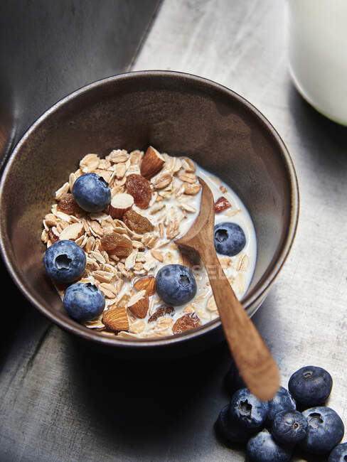 Bowl of muesli with raisins, almonds, blueberries and milk and wooden spoon — Stock Photo