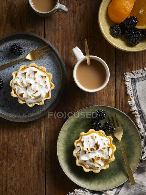 Tartas de merengue con bayas en platos por tazas de café - foto de stock