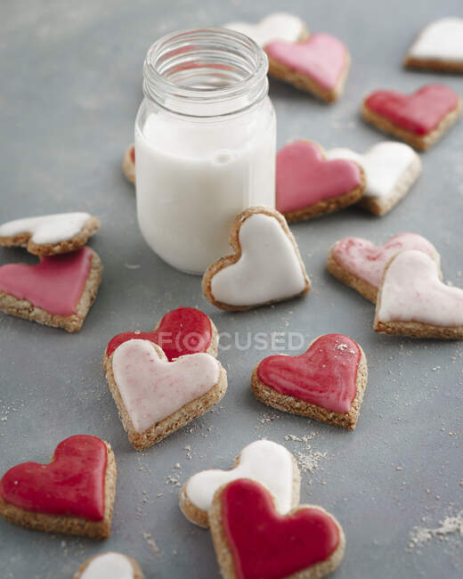 Pink, red and white heart-shaped biscuits with a glass of milk — Stock Photo