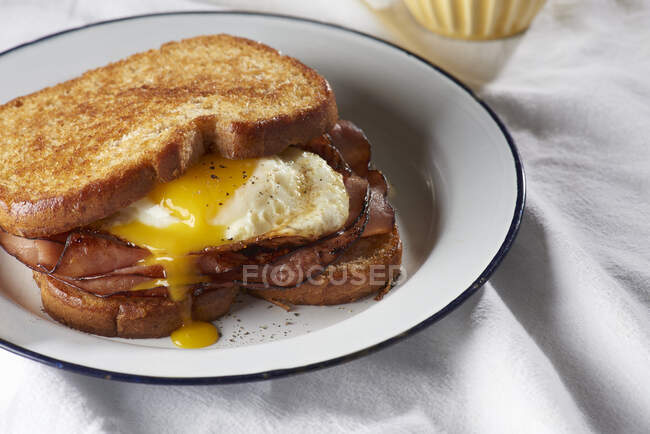 Sanduíche de ovo despedido com presunto fatiado e gema gotejamento — Fotografia de Stock