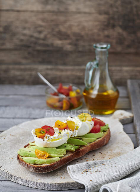Baguette half topped with avocado and burrata with tomatoes — Stock Photo
