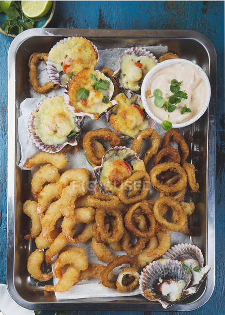 Bandeja caliente de mariscos: Anillos de calamares fritos, Osteones al horno y camarones fritos al horno con salsa - foto de stock
