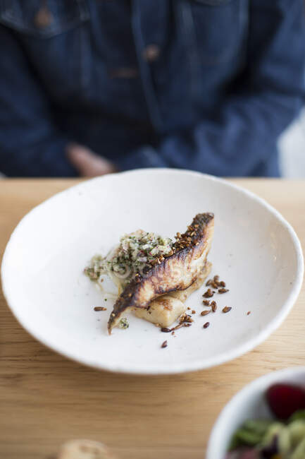 Pesce alla griglia in piatto con persona sullo sfondo — Foto stock