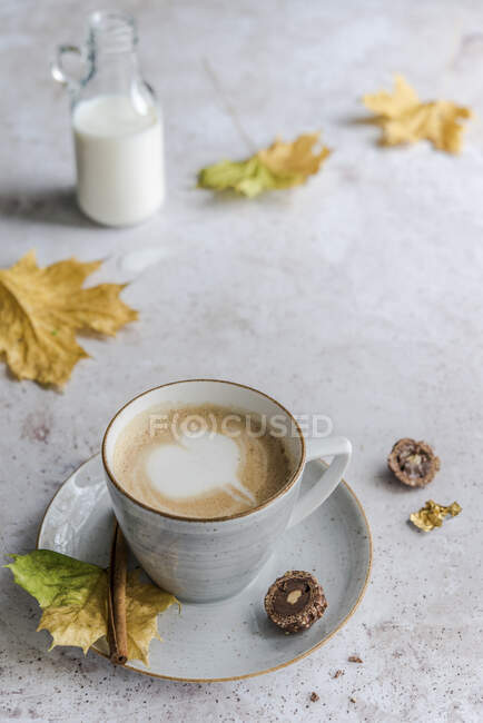Cappuccino con un corazón de espuma de leche rodeado de hojas de otoño - foto de stock