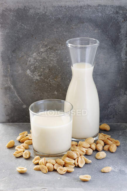 Jug and glass of nut milk and peanuts on stone background — Stock Photo
